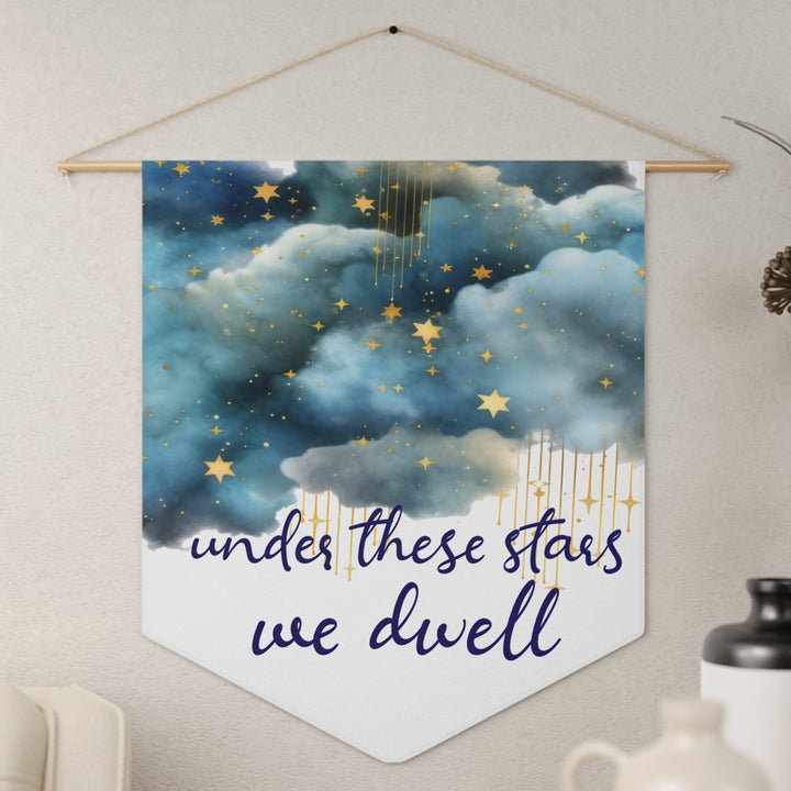 Decorative wall hanging with starry night design and text 'under these stars we dwell' on a neutral wall.
