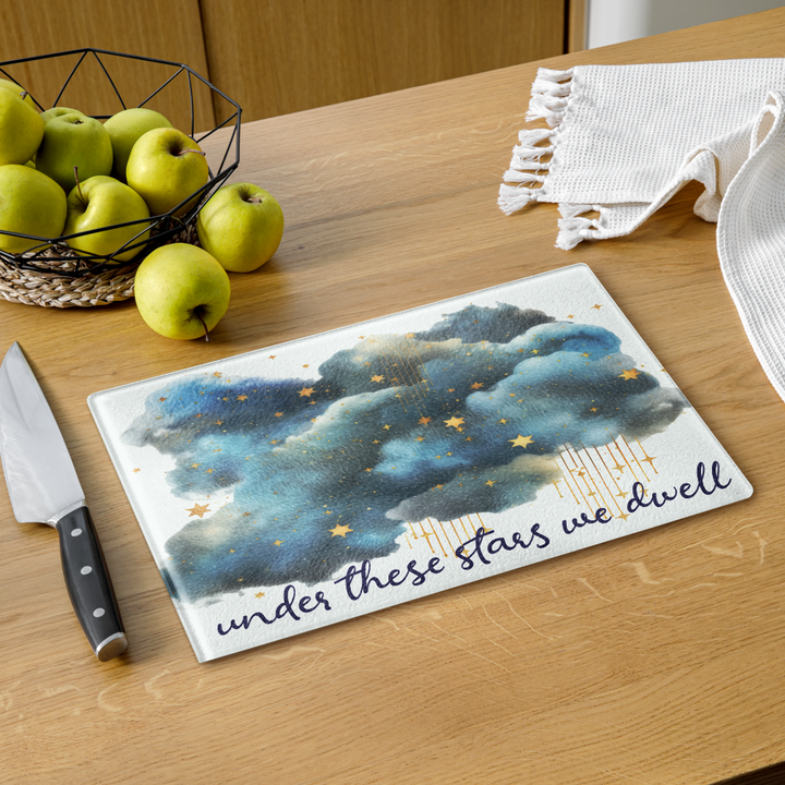 Decorative cutting board with starry night design and text on a kitchen counter with apples and a knife.